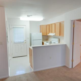 View of a compact apartment kitchen with light wooden cabinets and white appliances.