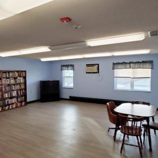 A cozy library reading room with bookshelves, tables, and chairs by the windows.