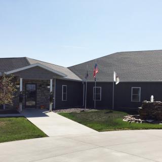 A single-story building with flags at the entrance, surrounded by a well-maintained lawn.