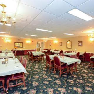 An elegant dining room with multiple tables and chairs, featuring a floral carpet and chandeliers.
