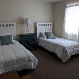 A simple bedroom featuring two twin beds with white bedding and a lamp between them.