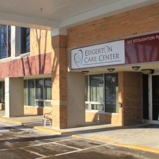 An exterior view of a clinic entrance with prominent signage and adjacent parking spaces.