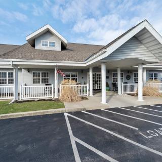 A front view of a building with a gable roof and an entrance supported by white columns, adjacent to a parking lot.