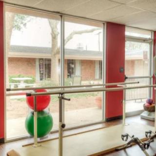A well-lit rehabilitation room featuring a ballet barre and colorful therapy balls, designed for physical therapy exercises.