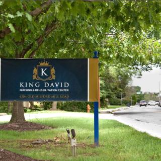 A sign for King David business consulting services beside a road lined with trees.