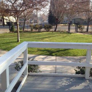 A sunny day in the park with a view of grass, trees, and a fenced pathway.