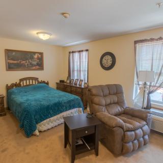 A cozy bedroom featuring a bed with a teal blanket, an armchair, and a side table near the window.