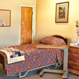 A cozy hospital room with a single bed, side table, and decorative quilt.