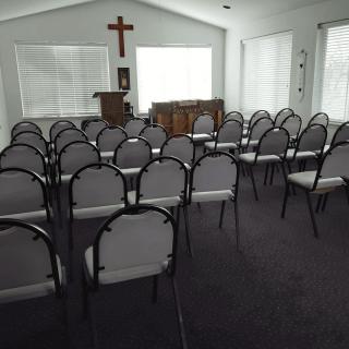 An interior view of a chapel with rows of chairs facing a cross and podium.