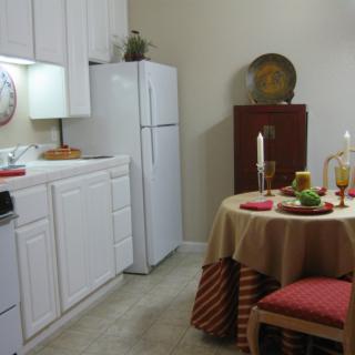 A cozy kitchen and dining area with a small round table set for a meal, featuring candles and decorative elements.