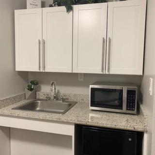 A compact kitchen area with white cabinets, a sink, a microwave, and a mini fridge.