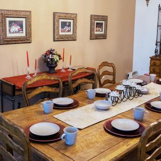 A cozy dining room with a table set for a meal, featuring plates, cups, candles, and floral decor.