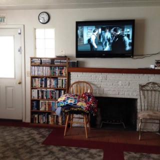 A cozy living room with a television mounted above a fireplace, flanked by a bookshelf and two chairs.