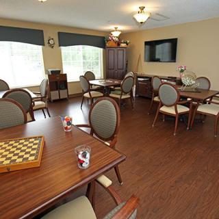A cozy games room with several tables and chairs, featuring a chessboard and a television.