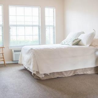 A bright and minimalist bedroom with white bedding and large windows letting in natural light.
