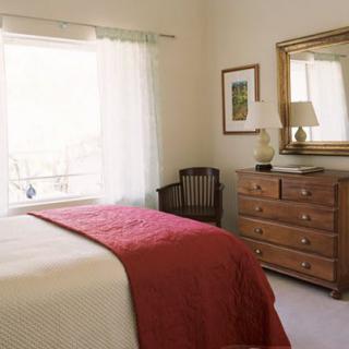 A cozy bedroom with a bed, dresser, and large mirror near a bright window.