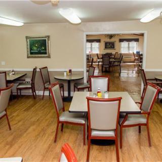An empty dining room with tables and chairs, featuring wood floors and simple decor.