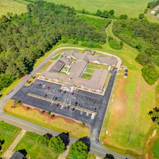 Aerial view of a building surrounded by lush greenery and a spacious parking lot.