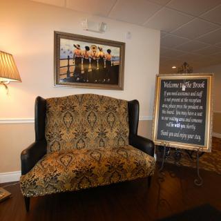 A cozy seating area with a patterned bench, a lamp, wall art, and a signboard displaying information.