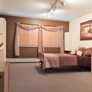 A warm-toned bedroom with a bed, carpet, and large windows with curtains.