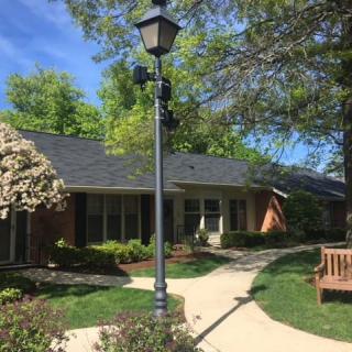 A serene view of a small building surrounded by trees and landscaping, featuring a pathway and a lamp post.