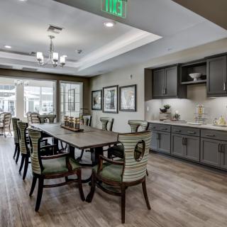 A modern dining room interior with a large wooden table, stylish chairs, and a kitchen area in the background.