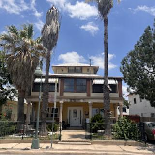 A charming two-story house surrounded by palm trees under a bright blue sky.