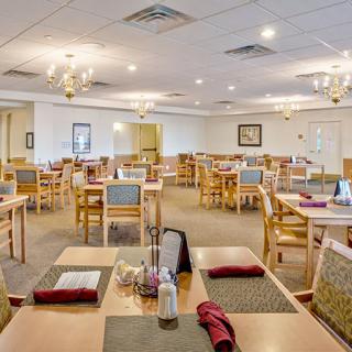 An empty restaurant dining area with neatly arranged tables and chairs, featuring chandeliers and table settings.