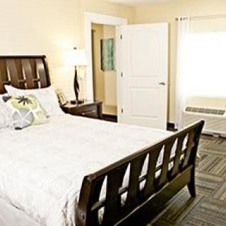 A cozy bedroom interior with a wooden bed, bedside lamp, and open door.