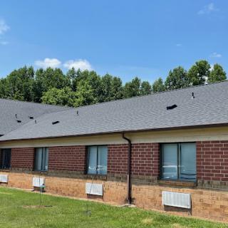 A view of a residential building featuring brick exterior, air conditioning units, and surrounded by greenery under a clear blue sky.