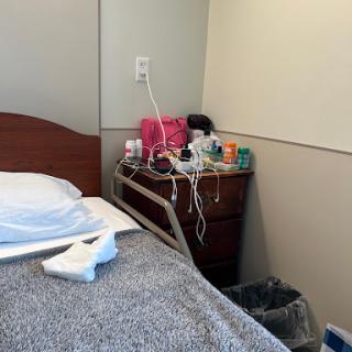 A view of a hospital patient room featuring a bed and a nightstand with various medical items.