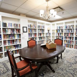 A cozy library room with bookshelves lining the walls, a wooden table, and chairs under a chandelier.