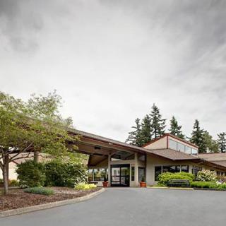 A building entrance surrounded by trees and landscaping under a cloudy sky.