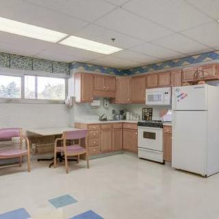 A simple kitchen and dining area with wooden cabinets, a refrigerator, stove, microwave, table, and chairs.