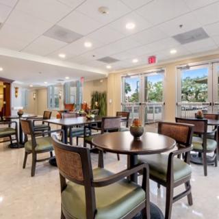 A bright and spacious dining area with multiple tables and chairs, featuring large windows allowing natural light to fill the room.