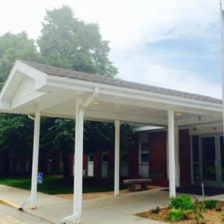 A building entrance with a covered walkway surrounded by trees.