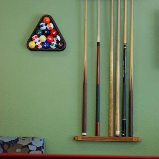 A collection of billiard cues and a rack of balls hanging on the wall in a game room.