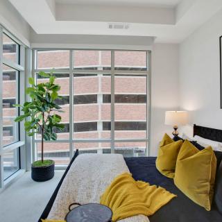 A modern bedroom with large windows, natural light, and yellow accent pillows.