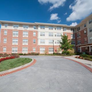 A modern residential apartment building with a brick facade, surrounded by landscaping under a clear blue sky.