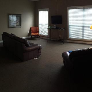 A dimly lit living room with sofas, a chair, and a television near large windows.
