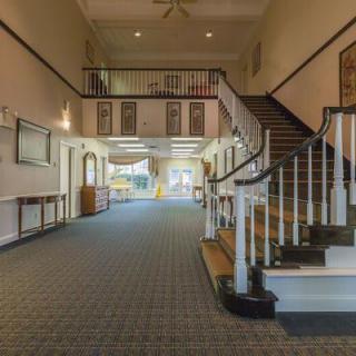 A spacious interior hallway featuring a staircase with a wooden banister and carpeted flooring.