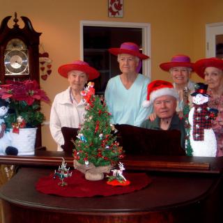 A group of people in festive hats gathered around a piano decorated for Christmas.