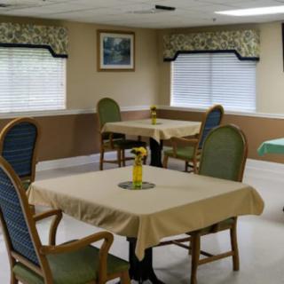 A dining area with neatly arranged tables and chairs, featuring window blinds and decorative elements.