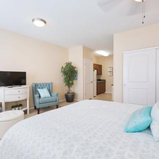 A bright and cozy bedroom with a large bed, a chair, a TV on a stand, and decorative elements.