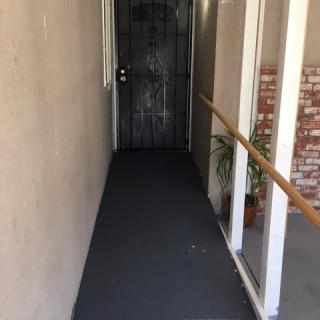 A narrow corridor with a metal door at the end, featuring a handrail and potted plant.