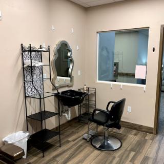 A neatly organized hair salon workspace with a barber chair, mirror, and shelving.