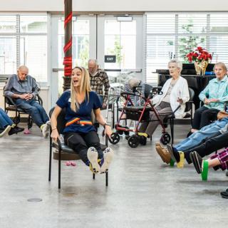A group of seniors participating in a seated exercise class indoors.