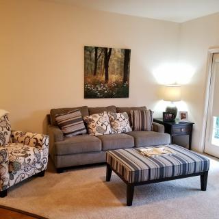 A cozy living room with a sofa, armchair, and striped ottoman, complemented by wall art and a warm lamp.