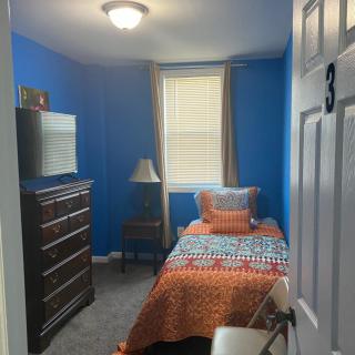 A cozy single bedroom with blue walls and a colorful bedspread.