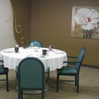 A small dining area with a round table set for four, featuring teal chairs and a floral painting on the wall.
